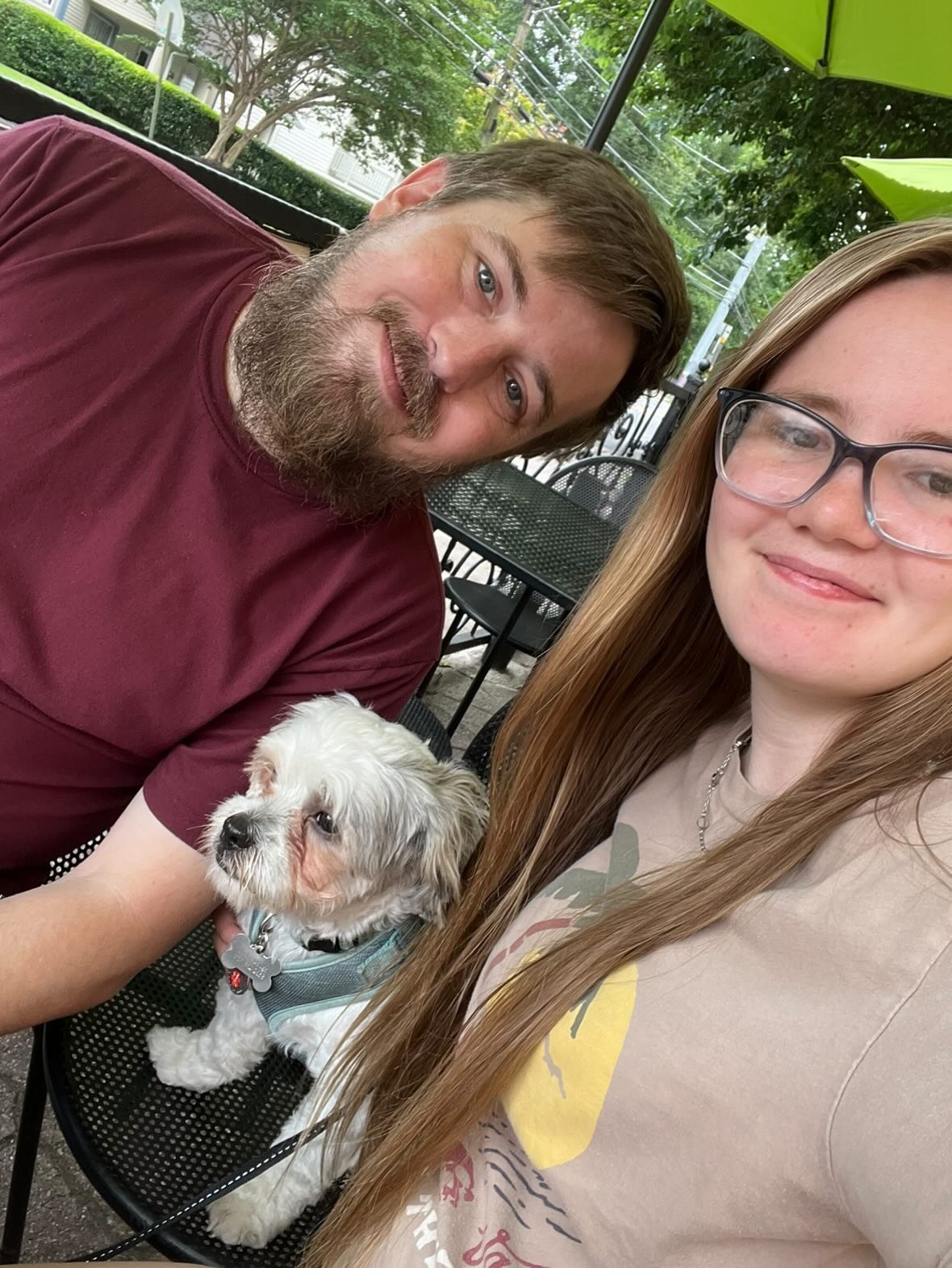 Nick and Libby sitting outdoors at a patio table with their small white dog