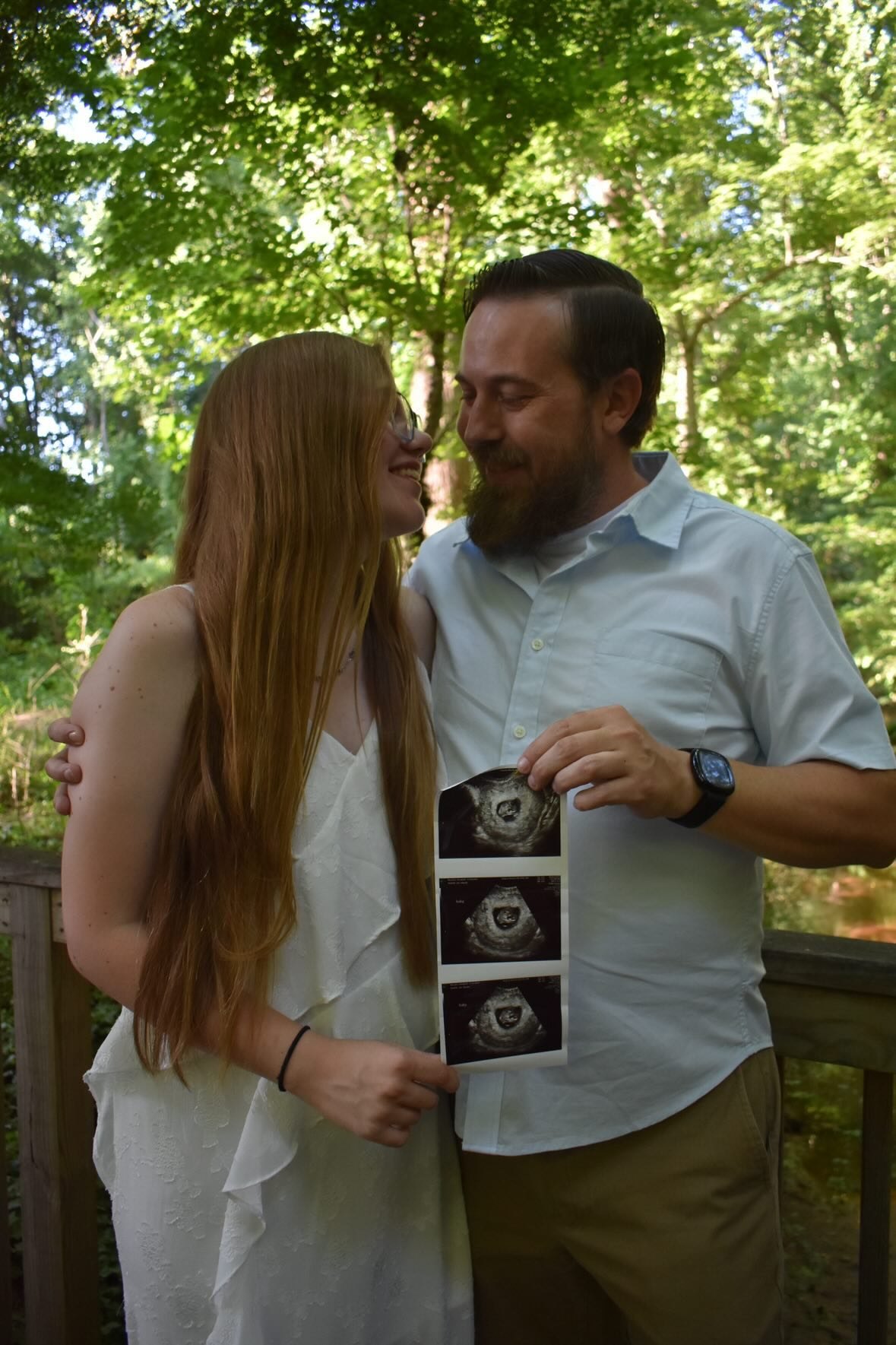 Nick and Libby standing together outdoors and holding sonogram photos