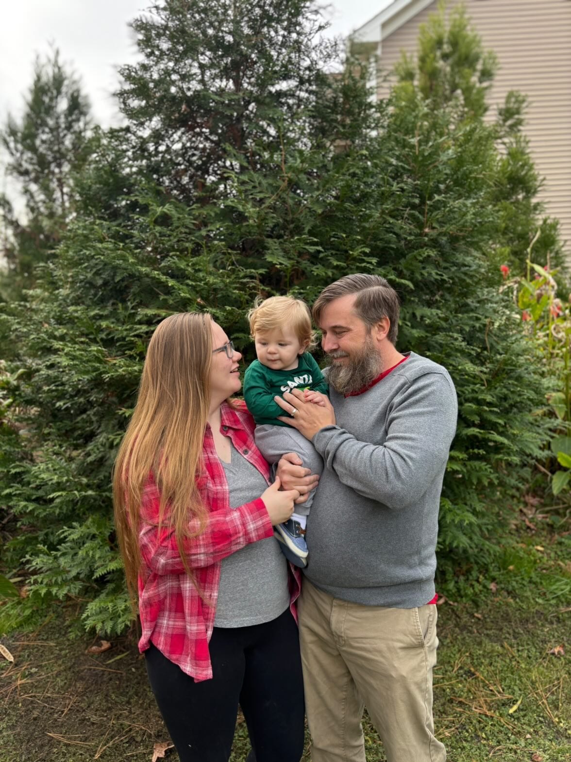 Nick and Libby holding their child outdoors in front of greenery