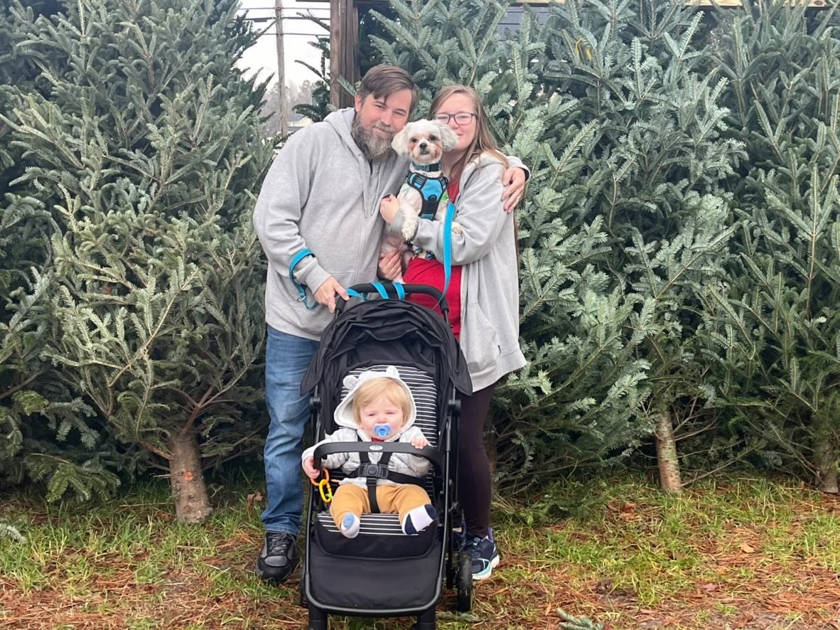 Nick, Libby, their child, and their dog at a Christmas tree lot